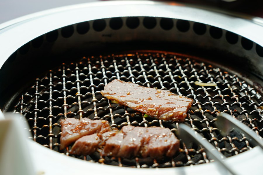 Tongs turning slices of beef on a tabletop charcoal grill