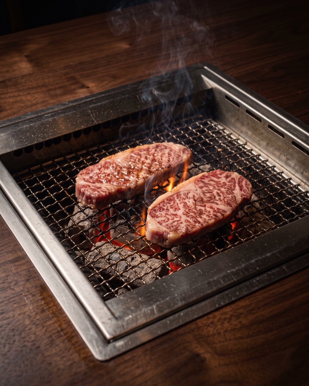 Two thick cuts of marbled wagyu searing on a wire grill above glowing charcoal