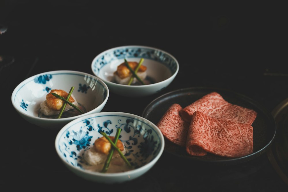 Small blue-and-white ceramic bowls beside marbled beef on a dark table